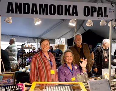 Opal Stall at the Opal FestivaL. Three people standing smiling under a sign titled 'Andamooka Opal'.